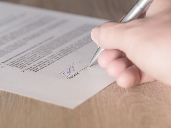 Hand unterschreibt ein Dokument mit einem Stift. Das Bild verweist auf die Dienstleistungen des Fleischerhandwerks.