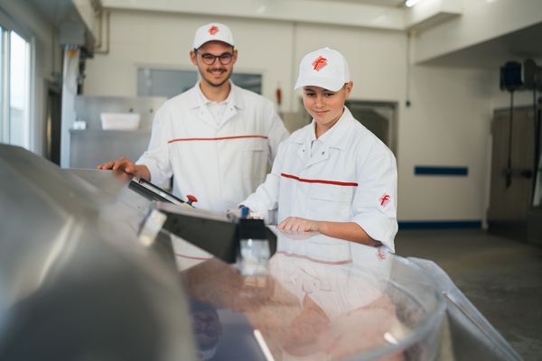 Zwei Fachkräfte in weißer Arbeitskleidung arbeiten gemeinsam im Produktionsbereich eines Fleischereibetriebs. Das Bild verweist auf den Pressebereich des Fleischerhandwerks.